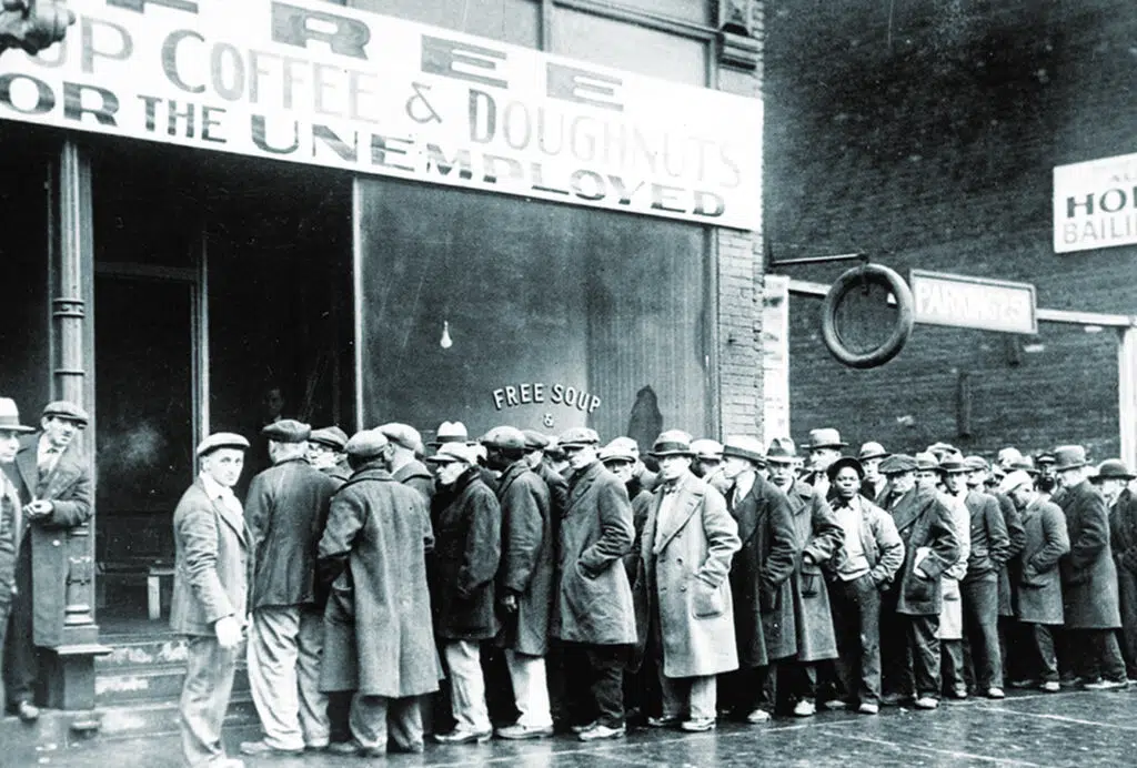 Unemployed men queue outside a soup kitchen opened in Chicago by Al Capone during The Great Depression. The storefront sign reads ‘Free soup, coffee and doughnuts for the unemployed’.