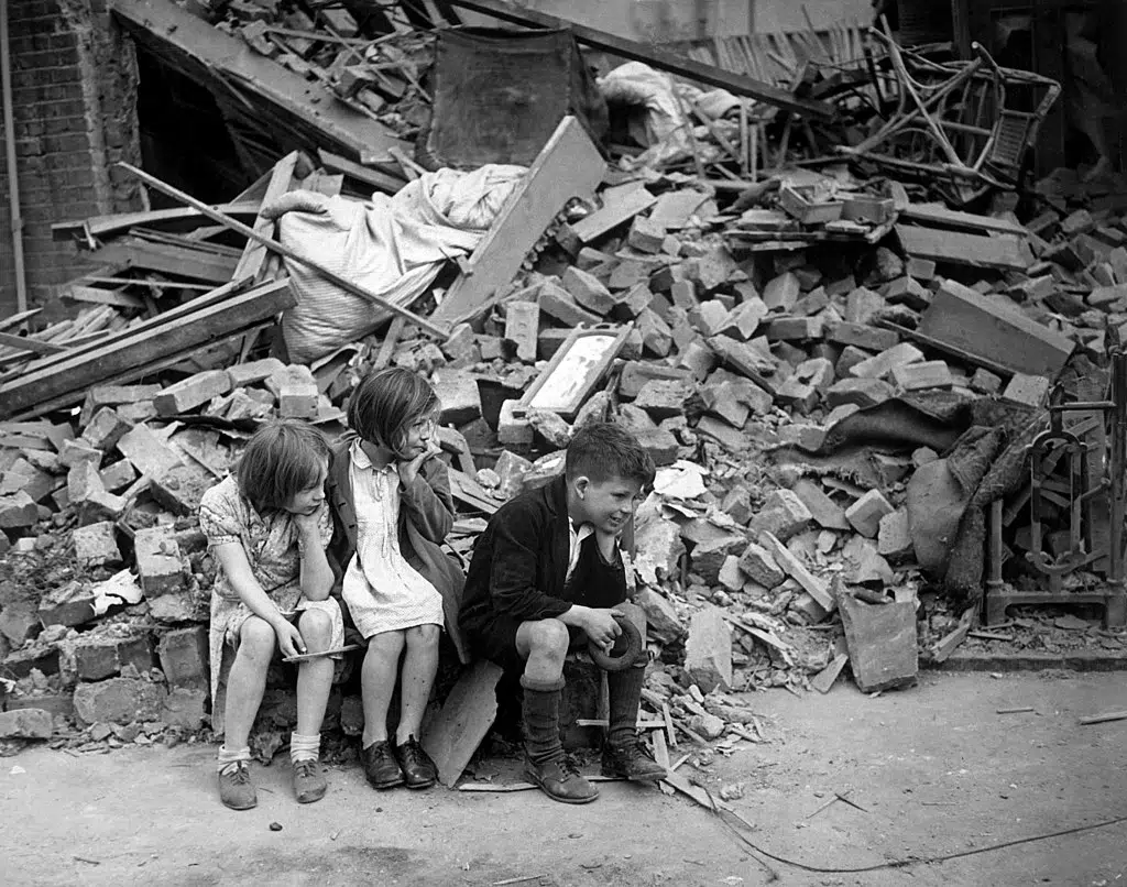 The blitz World War 2 Children in 1940s London sitting in the rubble after a bomb has hit